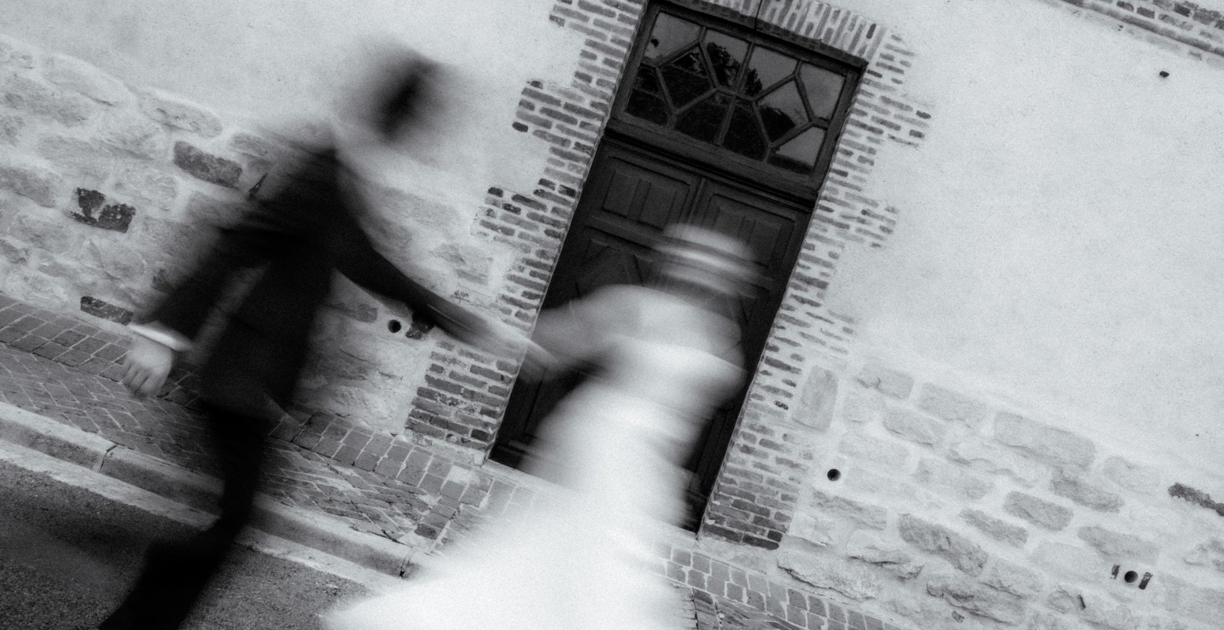 Les mariés en mouvement devant une porte ancienne, en noir et blanc
